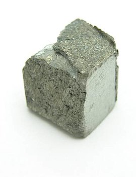 Roughly cube shaped piece of dirty grey metal with an uneven superficial structure.
