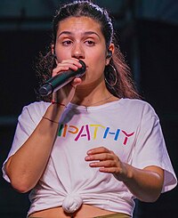 Alessia Cara in a white top that spells out the word "Empathy", singing into a microphone