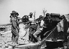Telanjang dada laki-laki di bungkuk topi dan celana berdiri dengan besar potongan artileri, siap untuk memuat shell.