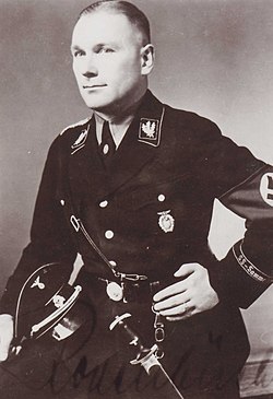 SS-Gruppenführer Alfred Rodenbücher omkring år 1938. På vänster bröstficka sitter Braunschweigmötets utmärkelse och från bältet hänger SS Hedersdolk. Titeln på vänster ärmelband är ”SS-Sammelstelle”.