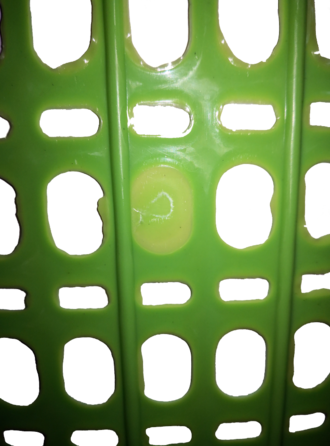 Flash, center, on a molded plastic laundry basket. Plastic has filled an area that should be an empty space, probably by seeping through a gap where the molds were not clamped sufficiently close together. Flashes di bakul.png