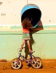 Girl balancing on bike to talk on a payphone, Brazil