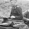 The head e shoulders of a man, shown from the side. He wears a black military uniform e cap, e an Iron Cross displayed at the front of his dark uniform collar