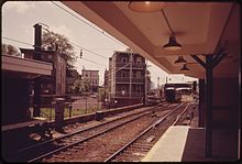 An outbound train approaches Wood Island in 1973 MBTA (METROPOLITAN BOSTON TRANSIT AUTHORITY) TRACKS CUT ACROSS NEPTUNE ROAD - NARA - 548475.jpg