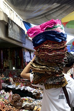 A textiles vendor carrying sarongs through Pasar Ubud, Bali