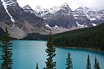 Lake and forest in front of high rocky mountains with snow.
