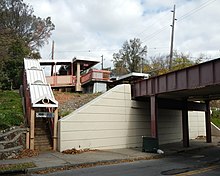 Cream-colored concrete abutment gives vertical support to both the small iron rail bridge and earthen fill of the bridge approach embankment at Old Town Station Staten Island Railway - Staten Island, New York Old Town Road SIRT SB stair jeh.jpg