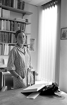 Рут Бейдер Гинзбург в домашнем халате в своём рабочем кабинете у себя дома. На столе лежит открытый журнал.