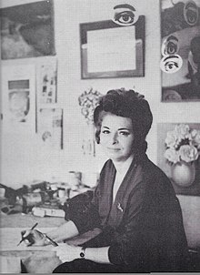 Rosa Rosenberg at her some studio in Mexico City, she is holding pens and brushes, and some of her artwork is visible in the background.