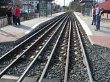 Hetzelfde, met perrons aan beide kanten. Van links naar rechts: rail 1 en 4: tramspoor perron links: rail 2 en 5; doorgaande goederenspoor; rail 3 en 6; tramspoor perron rechts. Trams kunnen hier elkaar niet kruisen. De tramsporen overlappen elkaar.