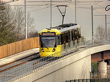A tram passing over a purpose built viaduct over the River Mersey on the newly opened Airport Line, in November 2014 Tram Across the Mersey, David Dixon, 4237015.jpg