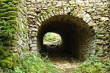 Enorme parede de pedra seca perfurada por um túnel abobadado áspero.