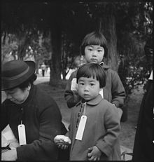 Hayward, California, May 8, 1942. Two children of the Mochida family who, with their parents, are awaiting an evacuation bus. The youngster on the right holds a sandwich given to her by one of a group of women who were present from a local church. The family unit is kept intact during evacuation and at War Relocation Authority centers where evacuees of Japanese ancestry will be housed for the duration.
(Photo by Dorothea Lange). Two Children of the Mochida Family, with Their Parents, Awaiting Evacuation Bus (3679508964).jpg