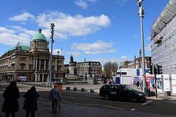 A general overlook of Victoria Square in Kingston upon Hull from the entrance of Princes Quay. To the left is Hull City Hall, behind a statue of Queen Victoria, poking out in the back is the Three Ships Mural of the soon-to-be-demolished former BHS building, and to the right is the Hull Maritime Museum, currently under tarpaulin for significant restoration work.