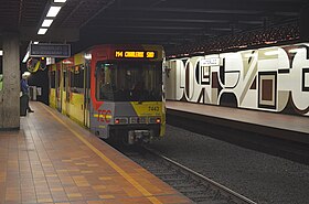 Voertuig dat het station verlaat.  Aan de muur een schilderij van André Goffin.