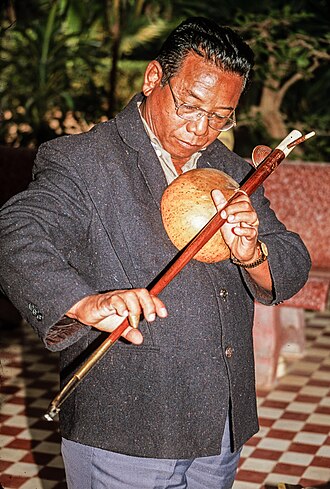 Wat Bo, Siem Reap, Cambodia. November 2001. Khmer Master Musician Yoeun Mek tries to play the one-stringed kse diev instrument for the first time. Mek met Sok Duch, who was the only surviving master of that instrument, teaching at Wat Bo in 2001. Yoeun Mek tries kse diev 2001.jpg