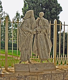 Sculpture de deux silhouettes élancées se rejoignant, à gauche Athénoras de profil avec sa grande barbe, à droite Paul VI avec un profil acéré ; la colombe du Saint-Esprit est représentée sur leurs mains s'étreignant
