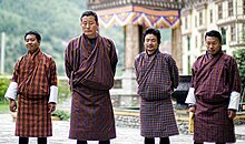 Four men outdoors in ruddy tartan gho robes, featuring four different patterns from very narrow to quite broad