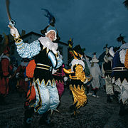 Fotografia de um grupo de pessoas vestindo trajes coloridos, à noite.