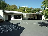 Fotografia a colori di edifici moderni alla fine di un cortile sul terreno del quale sono disegnati i giochi.