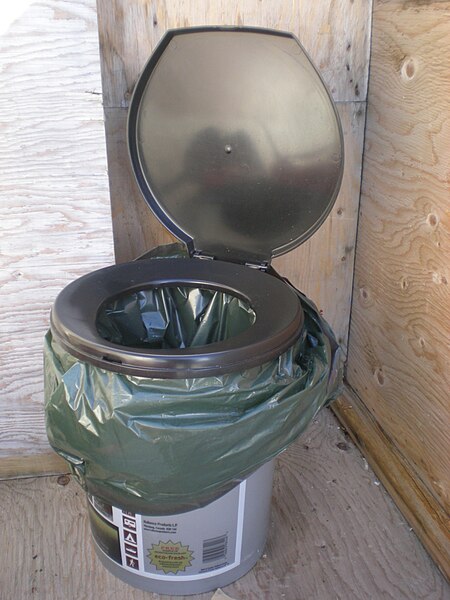 A plastic bucket fitted with a toilet seat for comfort and a lid and plastic bag for waste containment