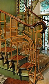 Photo en couleur d'un départ d'escalier avec rampe ouvragée en arabesques
