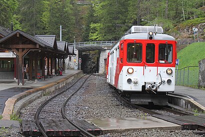 Boxy red-and-white train on double-track railway line next to station