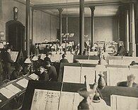 Black-and-white photo of a large room full of men reading newspapers on dedicated angled tables