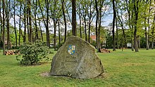 Findling in Parklandschaft. Eingemeißelt der Schriftzug „1105 – 2005“, darunter das Wappen der Gemeinde, darunter zweizeilig fortgesetzt der Schriftzug „900 Jahre / Kakenstorf“.