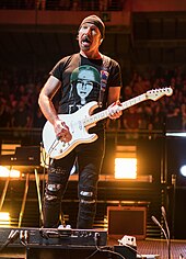 The Edge wearing a T-shirt bearing the likeness of his daughter Sian, who appears on the album cover The Edge wearing daughter shirt in Madrid on Experience and Innocence Tour 9-21-18.jpeg