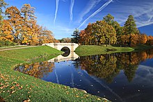 Dans un parc aux couleurs d'automne avec une belle étendue d'eau un pont tout blanc.