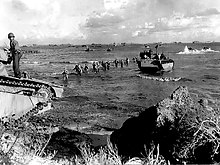 Men wade ashore from landing craft while LVTs move to and from the beachhead. In the background are ships that took part in the landing. Amphibious tractors move in and out - Tinian.jpg