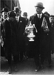 An elderly man holding the FA Cup