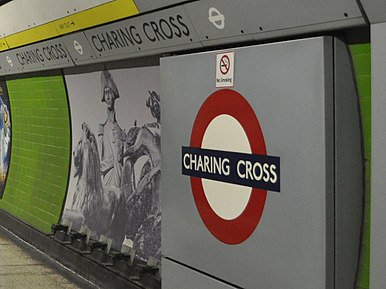 A platform wall: a panel contains the London Underground roundel with "CHARING CROSS" in the centre. A band contains the station name along the top of the wall. A decorative panel shows a photo-montage of Lord Nelson from the top of Nelson
