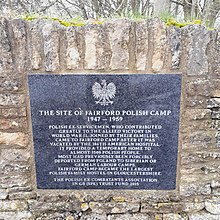 Black granite plaque with carved white upper-case lettering with a Polish Eagle Emblem at the top mounted within a Cotswold dry stone wall. It reads: The site of Fairford Polish Camp 1947-1959. Polish ex-servicemen, who contributed greatly to the allied victory in World War II, joined by their families, vacated by the 186th American Hospital. It provided a temporary home to almost 1500 Polish people. Most had previously been forcibly deported from Poland to Siberian or German labour camps. Fairford Camp became the largest Polish family hostel in Gloucestershire. The Polish ex-combatants Association in GB (SPK) Trust Fund 2015