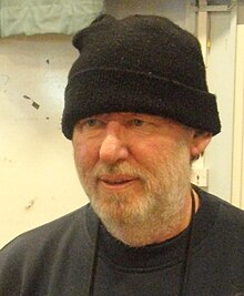 Un homme portant un bonnet et un pull noirs, ainsi qu'une barbe blanche.