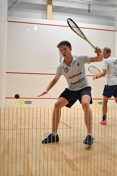 A squash player prepares to strike the ball with his racket