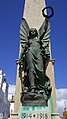 Affixed to the front of the monument, facing south, a female winged figure representing 'Victory', holding wreath aloft in left hand and lowered sword in right hand.