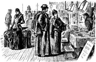 Jeune mariée et son époux devant un étal de livres dans le hall d'une gare, tous les deux en tenues de voyage avec pelisse, manteau et chapeau ; la dame pointe du doigt le livre qu'elle convoite ; plusieurs voyageurs s'affairent derrière eux avec leurs bagages, le tout en noir et blanc