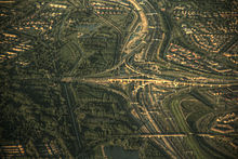 Aerial view of a traffic interchange with trees and houses in the rest of the image