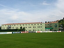 Veduta di un prato, con un edificio allungato sullo sfondo.