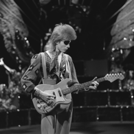 A black and white photo of David Bowie dressed as his Halloween Jack character, playing the guitar.