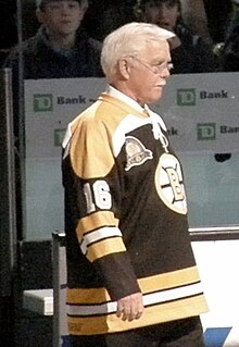 Photo de Sanderson de profil, cheveux blancs et lunettes sur le nez, portant le maillot numéro 16 des Bruins.