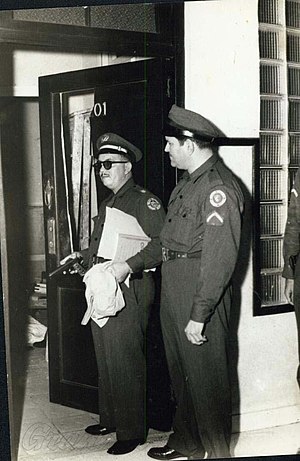 Havana police at the door of apartment 201. The policeman with the glasses appears to be Lt. Colonel Esteban Ventura Novo. El capitan Glery Hernandez de la 6ta Estacion de policia frente a la puerta destrozada del apartamento donde se habian refugiado los jovenes del DR.jpg