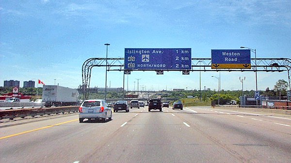 Typical overhead signage on Ontario's King's Highway network featuring an airport pictogram, distances to upcoming interchanges, and lane guidance