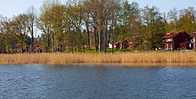 Photo taken from a body of water, showing tree-covered land with many red building on it