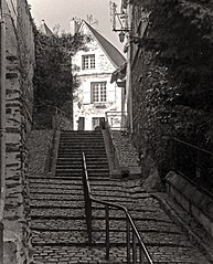 Sort / hvid fotografi af et hus i forlængelsen af ​​en trappe.