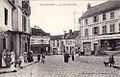 La rue Charles-de-Gaulle, vue depuis la place de la Mairie en direction du sud ; c'est une section de l'ancienne RN 16 pour Paris. La concentration des commerces confère à la scène une animation urbaine.