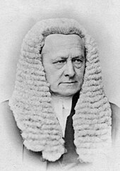 A man in a dated photograph in a suit with a white court wig. His expression does not portray an emotion.