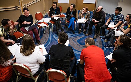 Participants are gathered on chairs in a circle. They are listening intently to one member of the group.